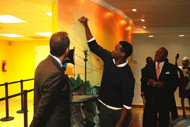BTC CEO Geoff Houston (left) and Minister of Public Works Neko Grant (right) look on as graphic artist Lamaro Smith signs the 27' x 8' mural he designed inside the newly renovated BTC Pioneers Way retail experience.