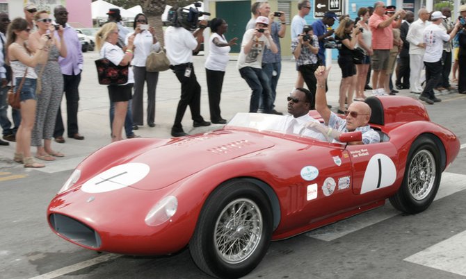 Minister of Youth, Sports and Culture Daniel Johnson (left) and Sterling Moss (right) drives off in Sterling Moss's car at the opening of Speed Week 2012 at Arawak Cay yesterday morning.