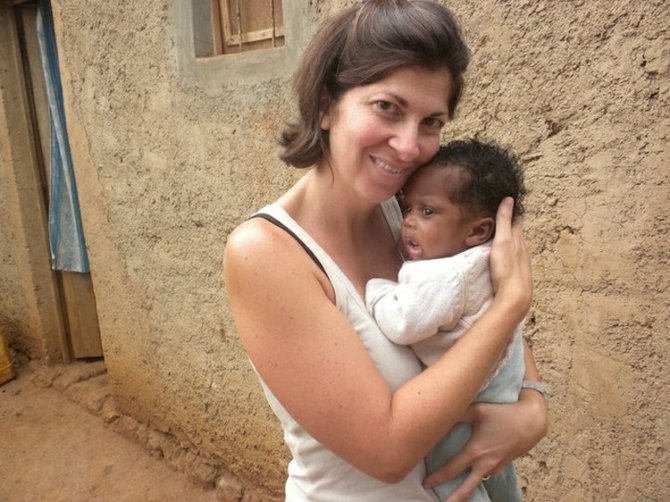 Tina holding a new born baby, the mother shared that her husband often cannot work because he suffers from severe head aches because of the trauma he received to the head from the genocide.