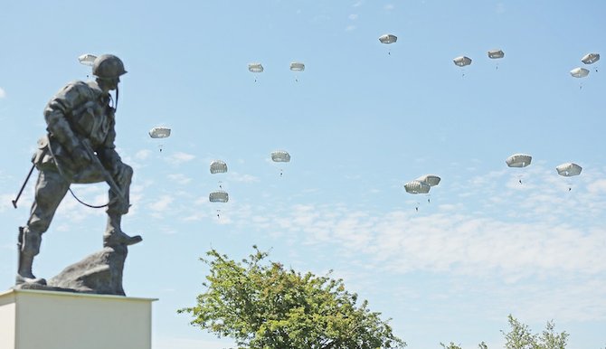 Paratroopers prepare to land near the Normandy village of Sainte Mere Eglise, western France, during a mass air drop on June 8, 2014, as part of commemorations of the 70th anniversary of the D-Day landing. Visible at left is the bronze sculpture Iron Mike, a monument dedicated to the American airborne soldiers who fought on D-Day.