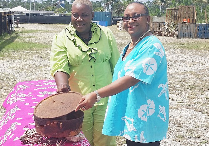 Angela Munnings, of the Freetown Heritage Association, and Elaine Smith of Ministry of Tourism, with the cast-iron pot that is used to cook on the fire half. Photo: Ministry of Tourism. 
