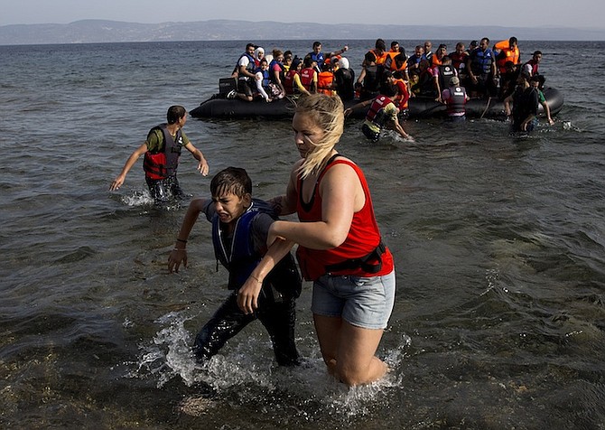 A volunteer helps a Syrian boy as he arrives with others at the coast on a dinghy after crossing from Turkey, at the island of Lesbos, Greece, on Monday. The island of some 100,000 residents has been transformed by the sudden new population of some 20,000 refugees and migrants, mostly from Syria, Iraq and Afghanistan. 
Photo: Petros Giannakouris/AP