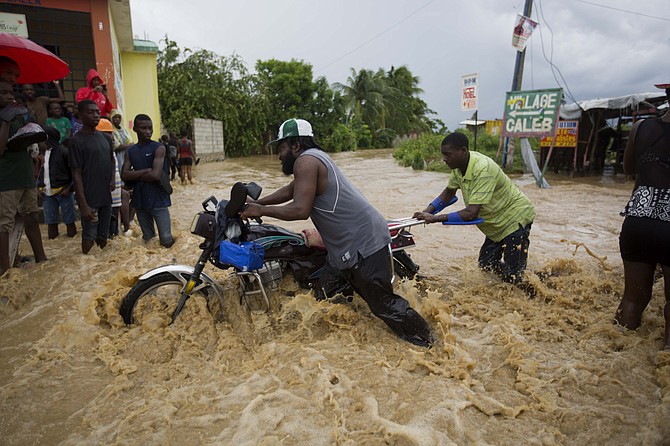 Men push a motorbike through a street flooded by a river that overflowed from heavy rains caused by Hurricane Matthew in Leogane, Haiti on Wednesday. Photo: Dieu Nalio Chery/AP