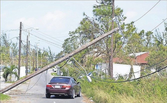 A car navigates its way past a precariously balanced pole amid downed power lines through Tayoo End off Marshall Road yesterday, as BPL came under fire for the slow pace of recovery efforts. 
Photo: Shawn Hanna/Tribune staff