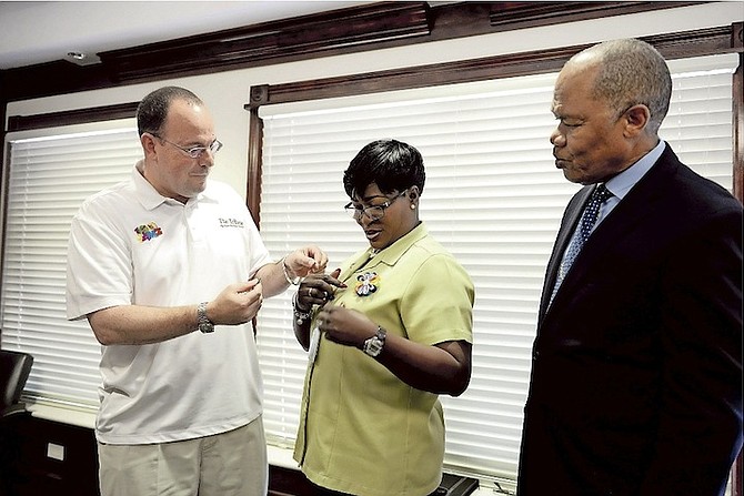 Veronica Ferguson receives her recognition pin from Kevin Darville, the Tribune Media Group’s special projects co-ordinator, as the February winner of the PHA Unsung Heroes award, watched by Herbert Brown, managing director of the Public Hospitals Authority.
 Photo: Shawn Hanna/Tribune Staff