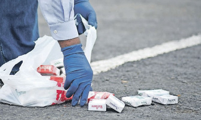 An investigator picks up cigarettes stolen from QVS Pharmacy at Seagrape Shopping Centre during an armed robbery where one suspect - a tenth grade student from RM Bailey Senior High School - was shot dead by police. Photo: Shawn Hanna/Tribune Staff