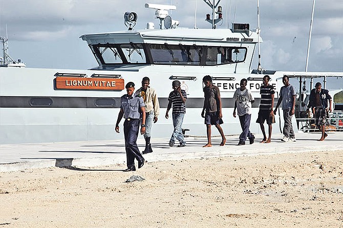 A marine escorts Haitian migrants off the patrol craft HMBS Lignum Vitae at the Coral Harbour Base shortly after they were apprehended early Monday morning. They were discovered in the central Bahamas on July 3. Photo: RBDF Public Relations Department