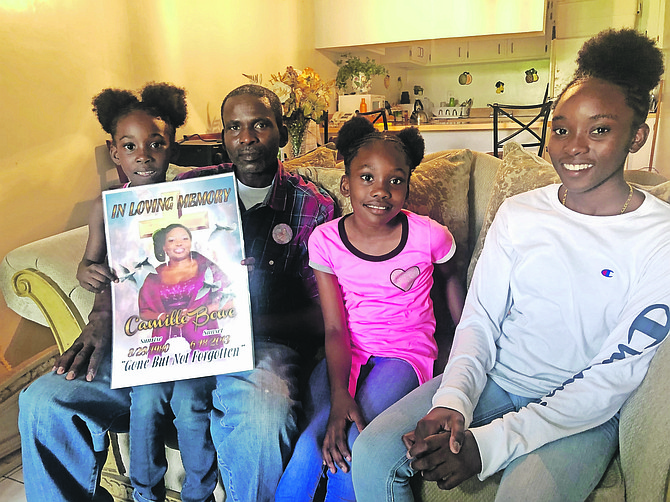 Leroy Bowe sits with his daughters, Moriah, six,  Le’Ajah, nine and Brianna, 13. Le’Ajah is holding a tribute poster of her mother Camille Williams-Bowe, who died at 32. “She might be gone but her spirit is always here, guiding and watching over us,” says her husband.