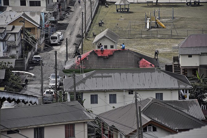 People clean volcanic ash from the red roof of a home after the volcano eruption in St Vincent.  (AP Photo/Orvil Samuel)