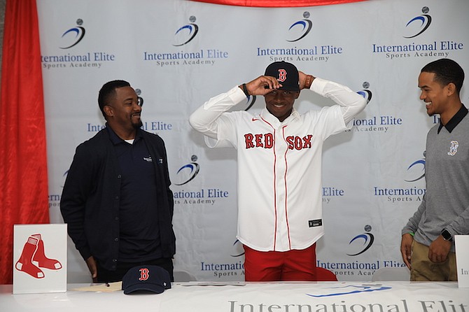 Chad Delancey puts on his Boston Red Sox cap as coach Albert Cartwright and Boston's Bahamian agent, Dominique Collie, look on. Photo by Trevere Saunders.