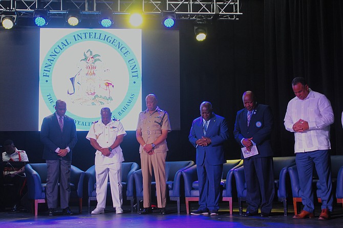 Prime Minister Philip Davis (third from right) bows his head for the opening prayer at the Financial Intelligence Unit MLRO Forum 2024. He is joined on stage by (L-R) Head of IT of FIU Darrington Rahming; Royal Bahamas Defence Force Commodore Raymond E. King; Police Commissioner Clayton Fernander; Mr Emrick Seymour, Director of FIU (right of PM); and Min. State of Economic Affairs Michael Halkitis. Photo: Shaquille Johnson